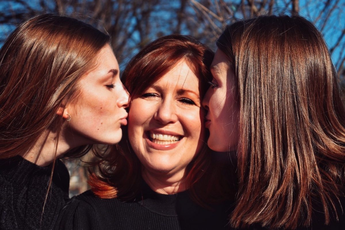 A mother being warmly hugged by her two teenage daughters, symbolizing connection, love, and family unity