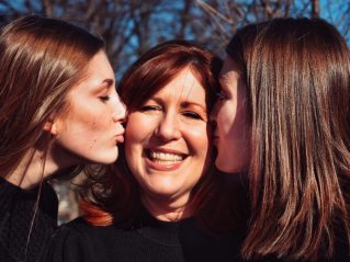 A mother being warmly hugged by her two teenage daughters, symbolizing connection, love, and family unity