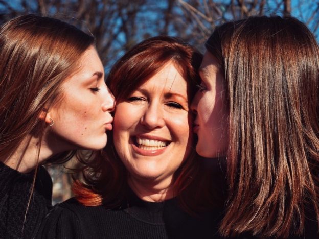 A mother being warmly hugged by her two teenage daughters, symbolizing connection, love, and family unity